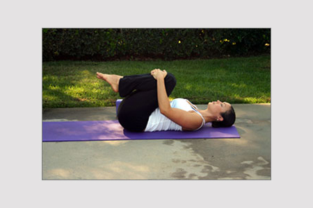 A woman on her back with her knees up and her hands wrapped round her knees - some sort of yoga stretch